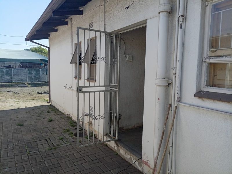 Rear exterior view of the building featuring a security gate, paved walkway, and visible wear on the exterior wall finish.