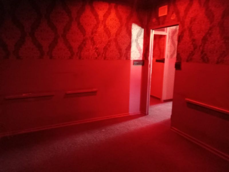 A dimly lit, empty hallway featuring patterned wallpaper and simple architectural finishes, requiring cosmetic updates to improve the overall aesthetic.