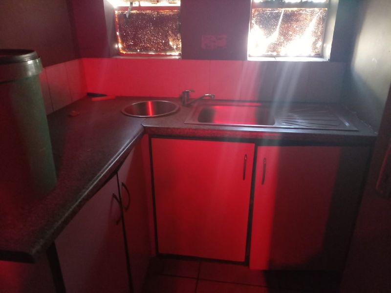 A small scullery or utility area featuring built-in cabinetry, a stainless steel sink, and a laminate countertop, requiring cosmetic updates.