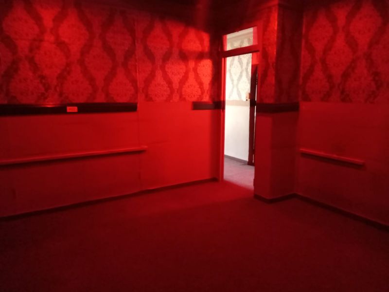 An empty interior room featuring patterned wallpaper and chair rail molding, currently illuminated by red lighting.