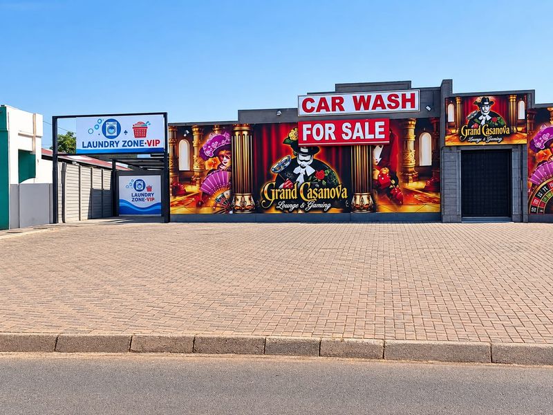 Front exterior view of a commercial property featuring paved parking, prominent signage for a car wash, laundry, and gaming lounge.