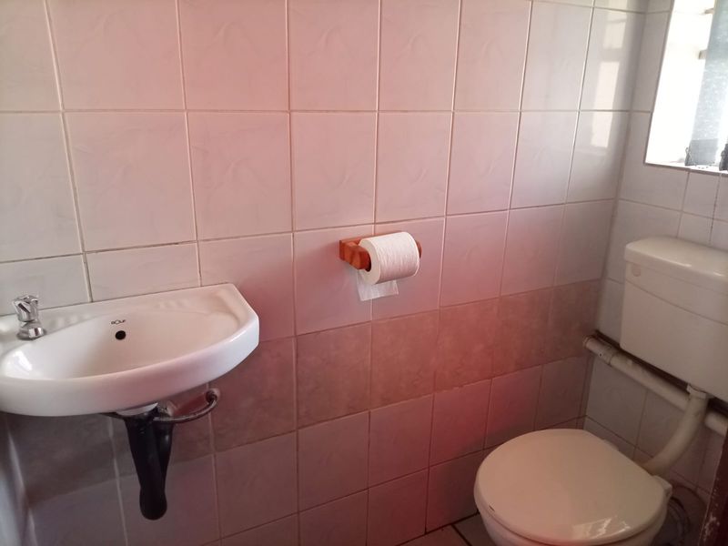 A compact bathroom featuring a wall-mounted basin and standard toilet with tiled walls. The space is functional but dated and requires cosmetic updates.