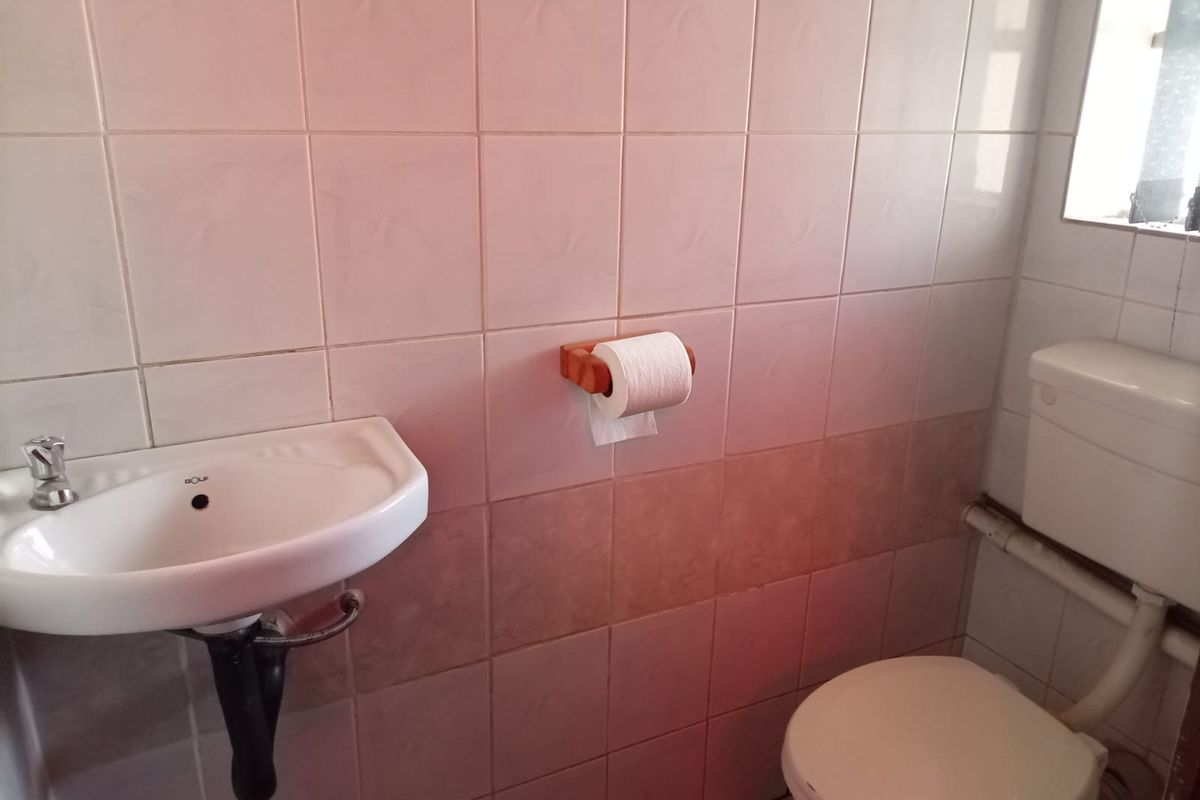 A compact bathroom featuring a wall-mounted basin and standard toilet with tiled walls. The space is functional but dated and requires cosmetic updates.