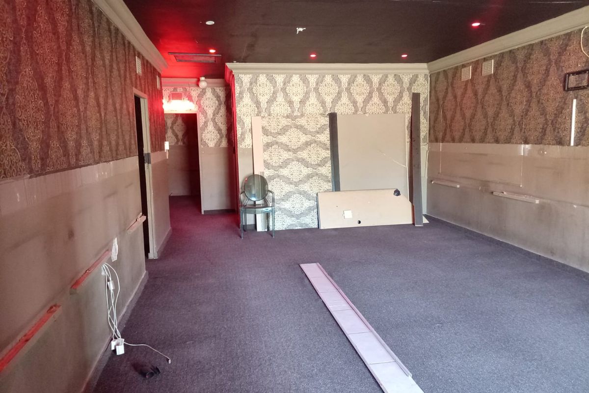 An empty commercial space featuring patterned wallpaper, dark carpeting, and recessed ceiling lighting, currently requiring cosmetic updates and repairs to wall finishes.