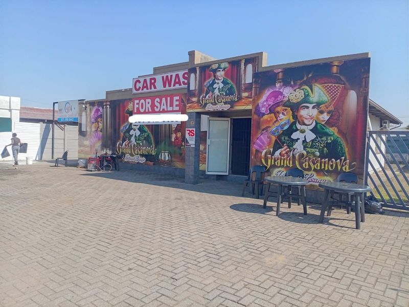 Front exterior view of a commercial property featuring paved driveway, security gate, and prominent signage for a car wash and lounge business.