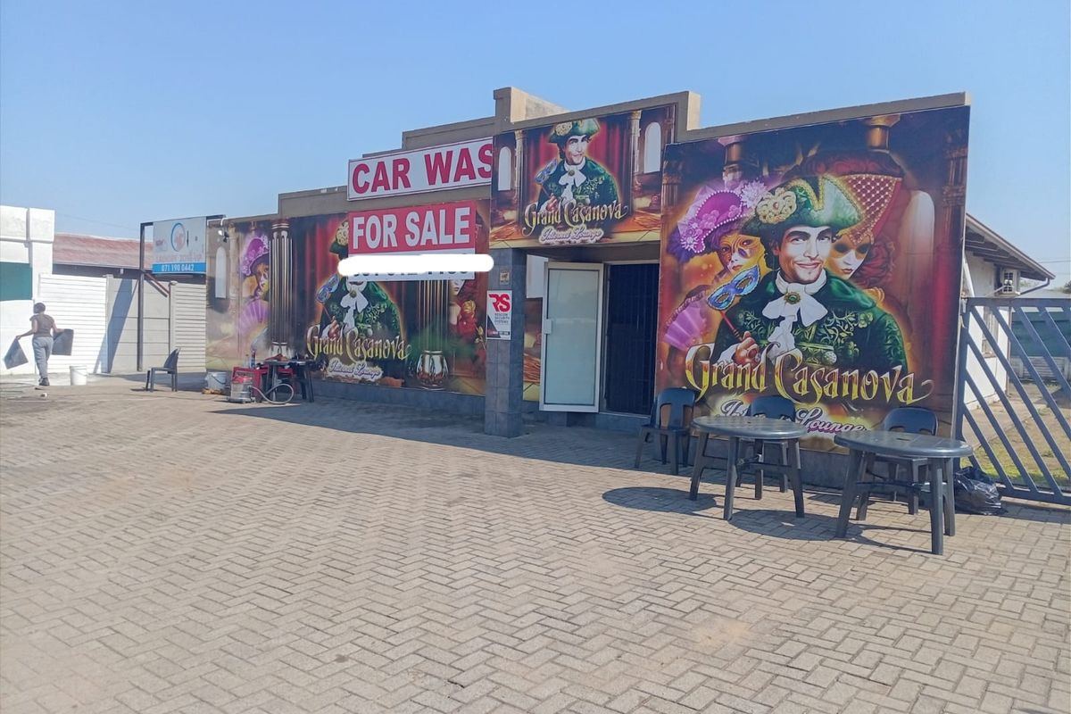 Front exterior view of a commercial property featuring paved driveway, security gate, and prominent signage for a car wash and lounge business.