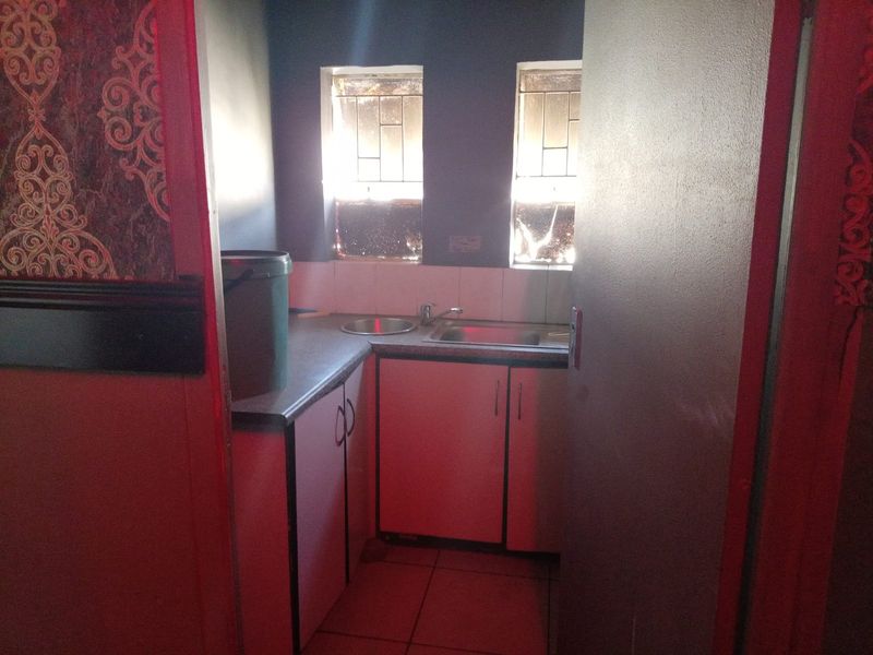 A compact scullery area featuring built-in cabinetry, a stainless steel sink, and tiled splashbacks, providing functional utility space.