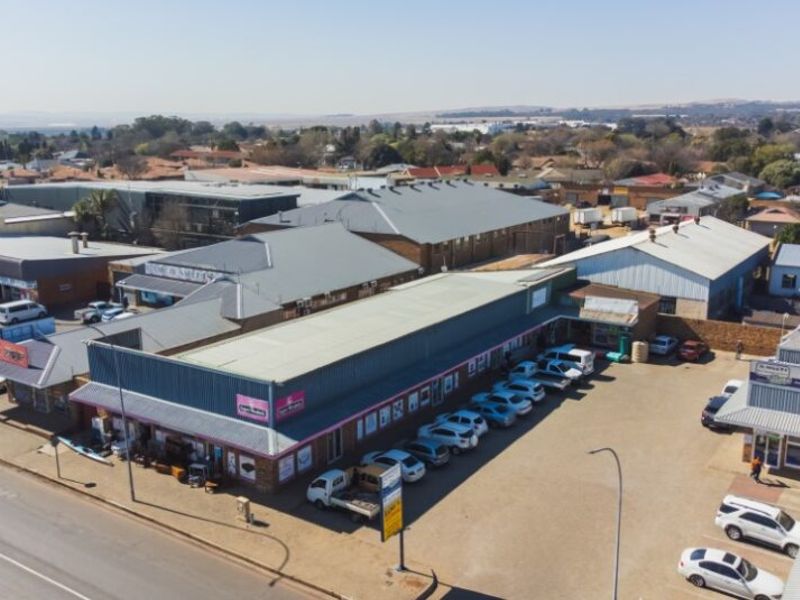 Aerial view of a commercial retail complex featuring multiple storefronts, metal roofing, and an expansive paved parking area.