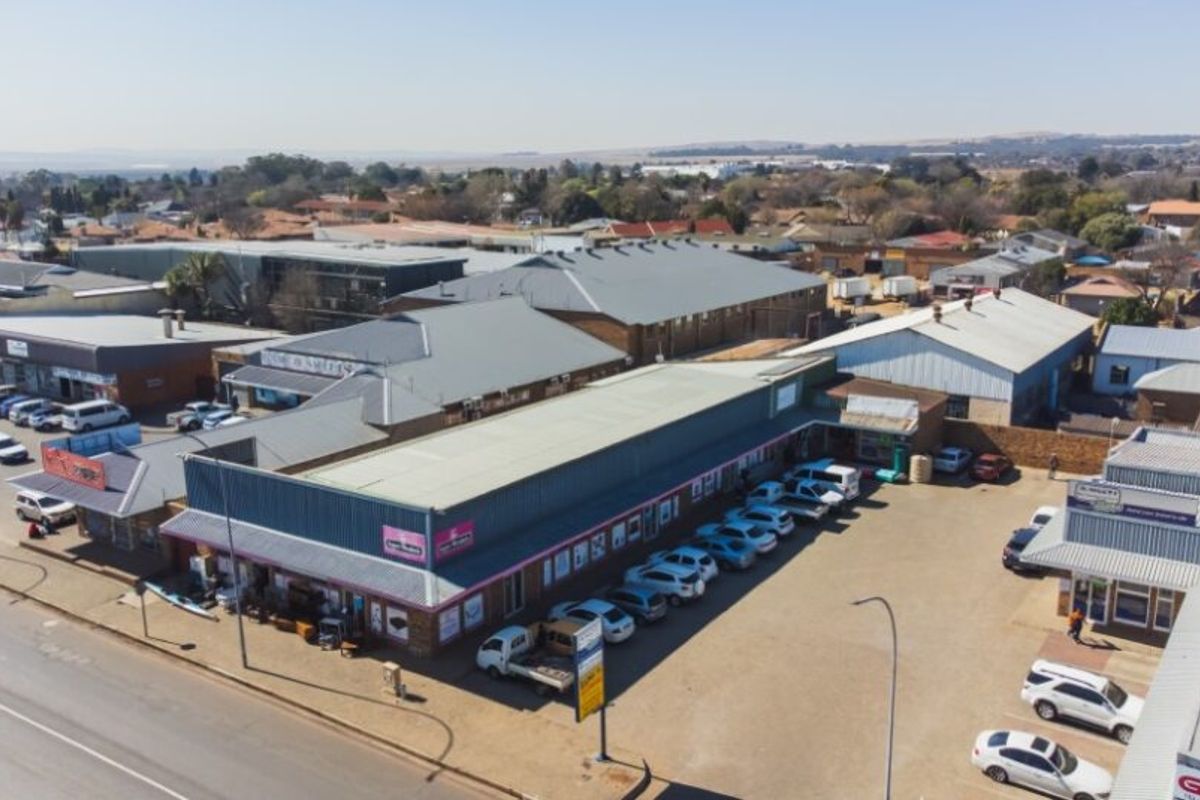 Aerial view of a commercial retail complex featuring multiple storefronts, metal roofing, and an expansive paved parking area.