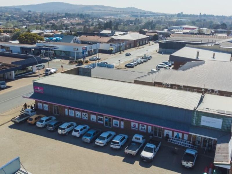Aerial view of a commercial retail property featuring a metal roof, storefront entrance, and an adjacent paved parking area in a suburban setting.