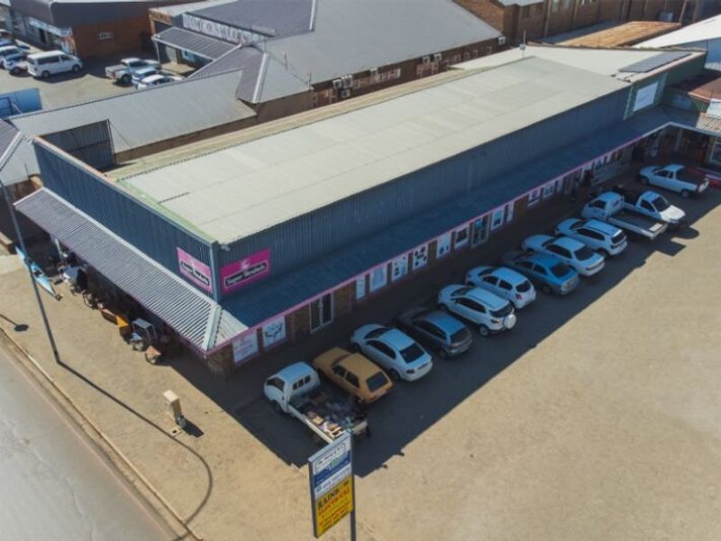 Aerial view of a commercial retail property featuring a large corrugated metal roof and an adjacent paved parking area.