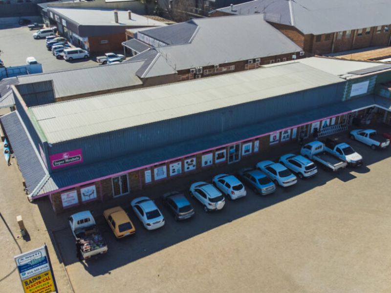 Aerial view of a commercial retail property featuring a large metal-roofed building with an adjacent asphalt parking area and street-level access.
