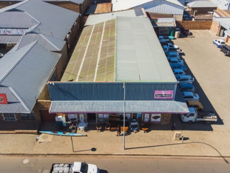 Aerial view of a commercial retail property featuring a corrugated metal roof, front awning, and adjacent paved parking area.