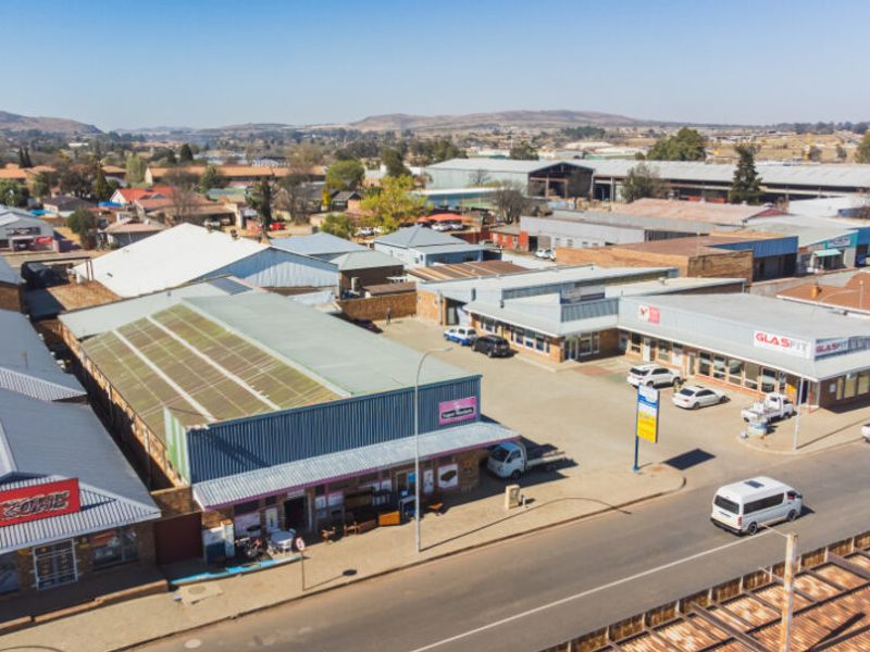 Aerial view of a commercial retail complex featuring multiple storefronts, metal roofing, and an adjacent paved parking area.