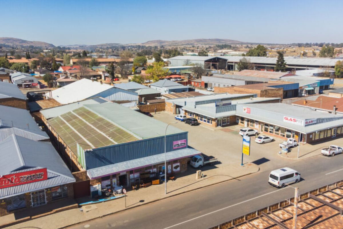 Aerial view of a commercial retail complex featuring multiple storefronts, metal roofing, and an adjacent paved parking area.