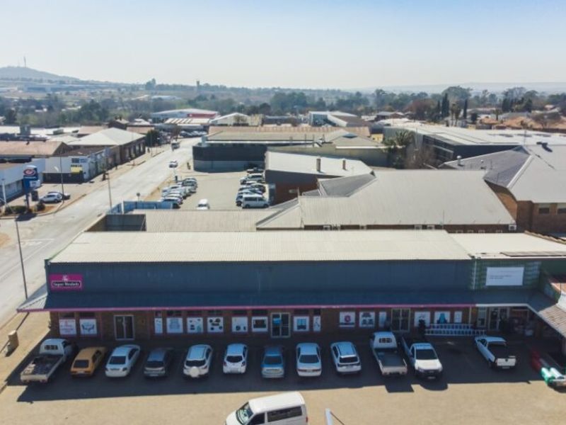 Aerial view of a commercial retail property featuring a metal roof, brick facade, and an adjacent paved parking area.