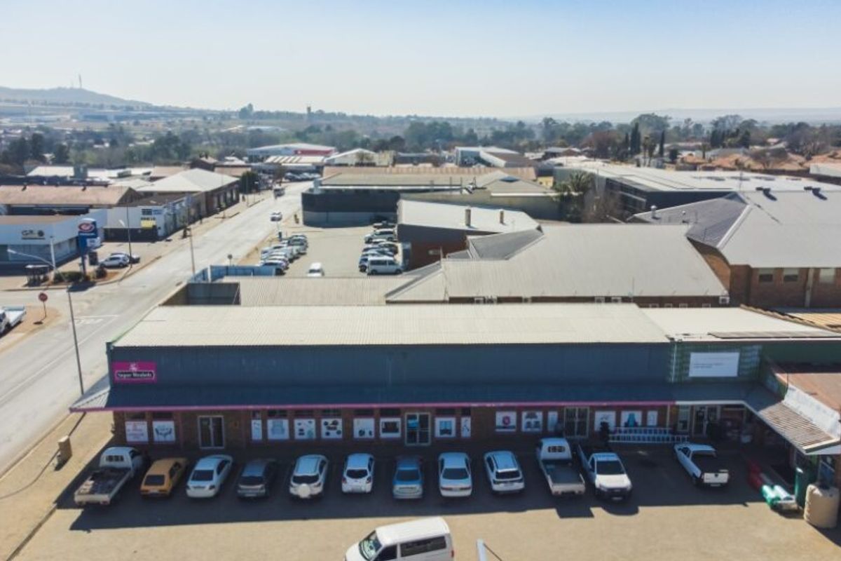 Aerial view of a commercial retail property featuring a metal roof, brick facade, and an adjacent paved parking area.