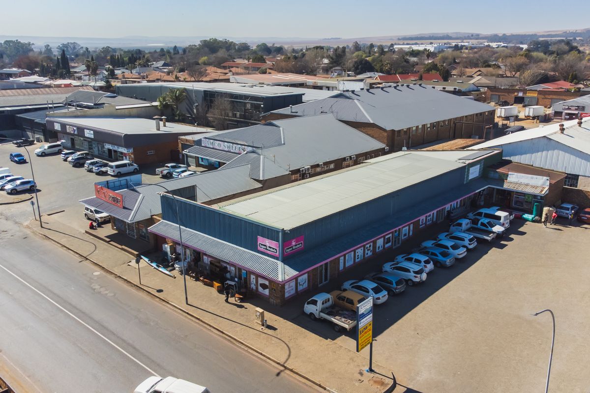 Aerial view of a commercial retail complex featuring multiple storefronts, metal roofing, and an extensive asphalt parking area.