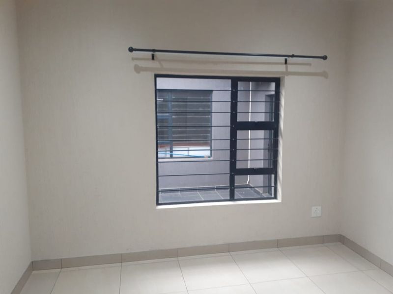 A clean, empty bedroom featuring neutral tiled flooring, an aluminium window with security bars, and a fitted curtain rod.
