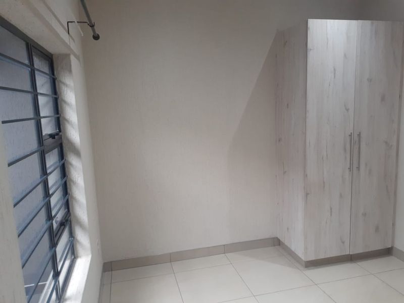 A clean, empty bedroom featuring neutral tiled flooring, a modern built-in wardrobe, and a window fitted with security bars.