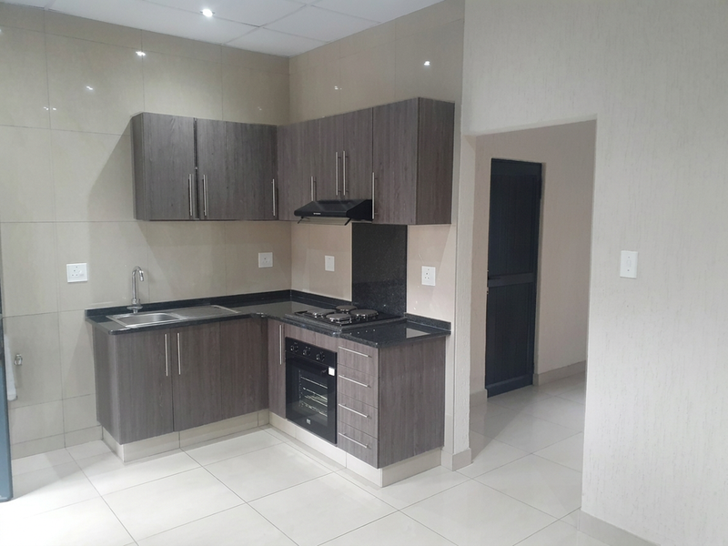 Modern kitchen featuring dark wood cabinetry, granite countertops, built-in oven, electric hob, extractor fan, and neutral tiled finishes throughout.