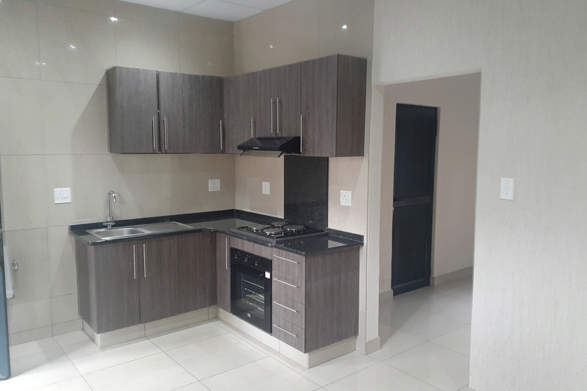 Modern kitchen featuring dark wood cabinetry, granite countertops, built-in oven, electric hob, extractor fan, and neutral tiled finishes throughout.