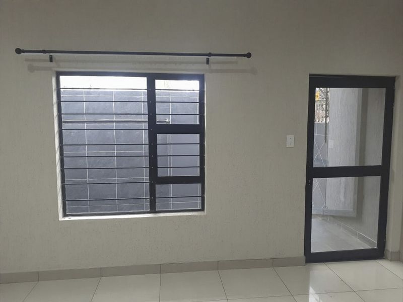 An empty interior space featuring tiled flooring, an aluminium window with security bars, and an aluminium door frame.
