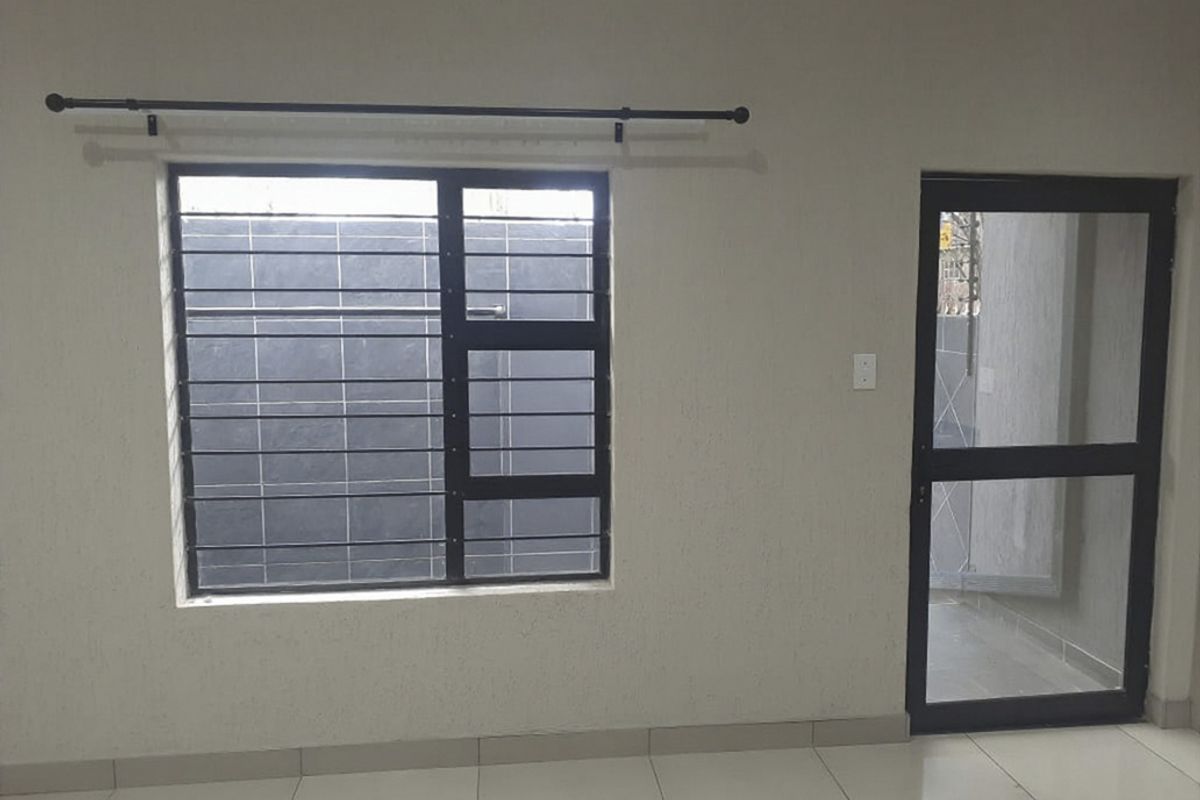 An empty interior space featuring tiled flooring, an aluminium window with security bars, and an aluminium door frame.