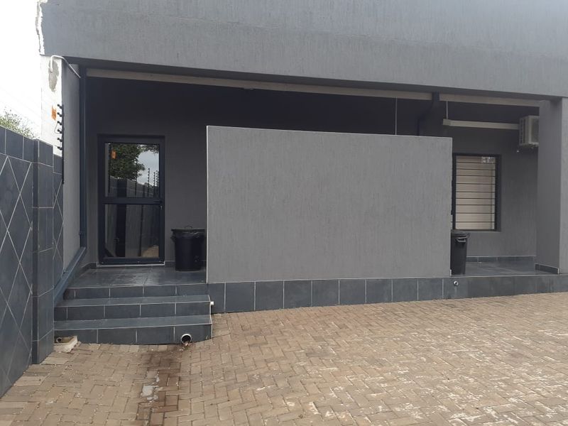 Commercial building exterior featuring a paved driveway, tiled entrance steps, modern grey facade, and aluminium window and door frames.