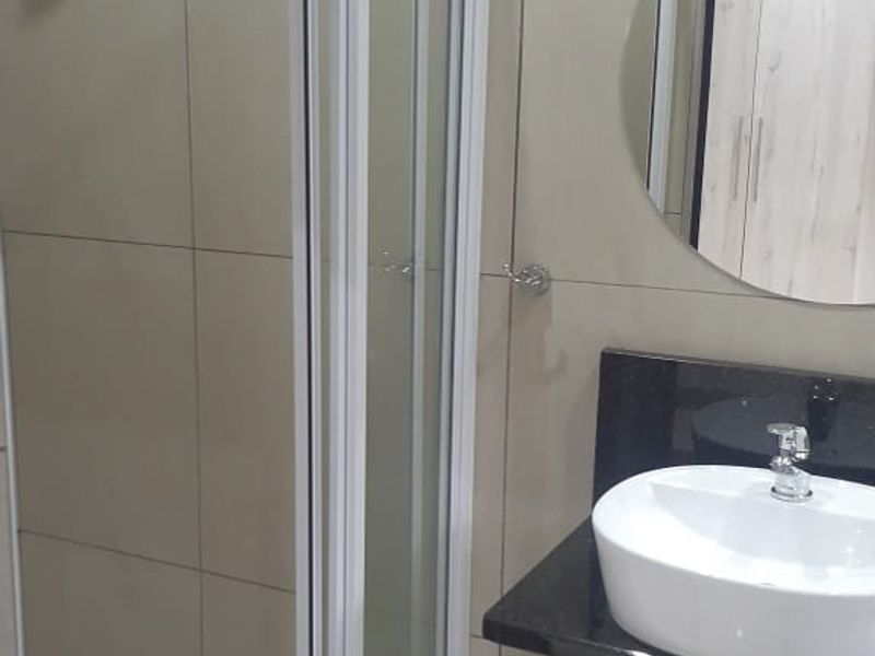 A modern bathroom featuring a glass-enclosed shower, wall-mounted basin with a granite countertop, and neutral wall tiling.