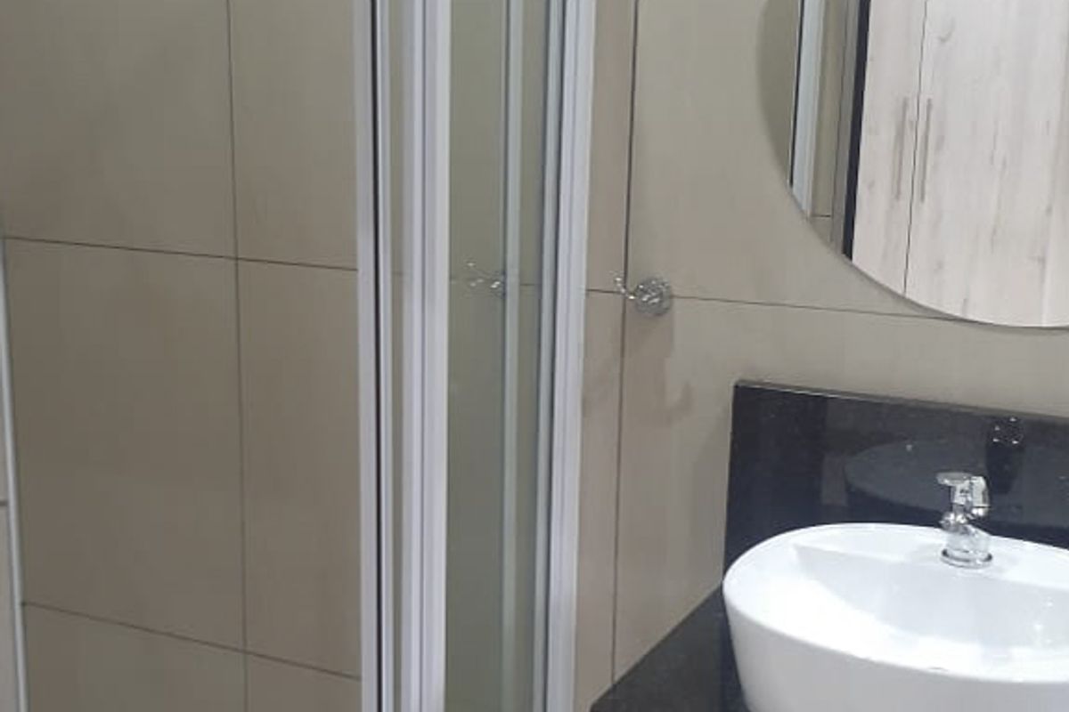 A modern bathroom featuring a glass-enclosed shower, wall-mounted basin with a granite countertop, and neutral wall tiling.