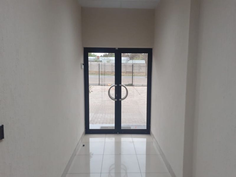 A clean and bright office entrance featuring double glass doors, neutral wall finishes, and polished floor tiles.