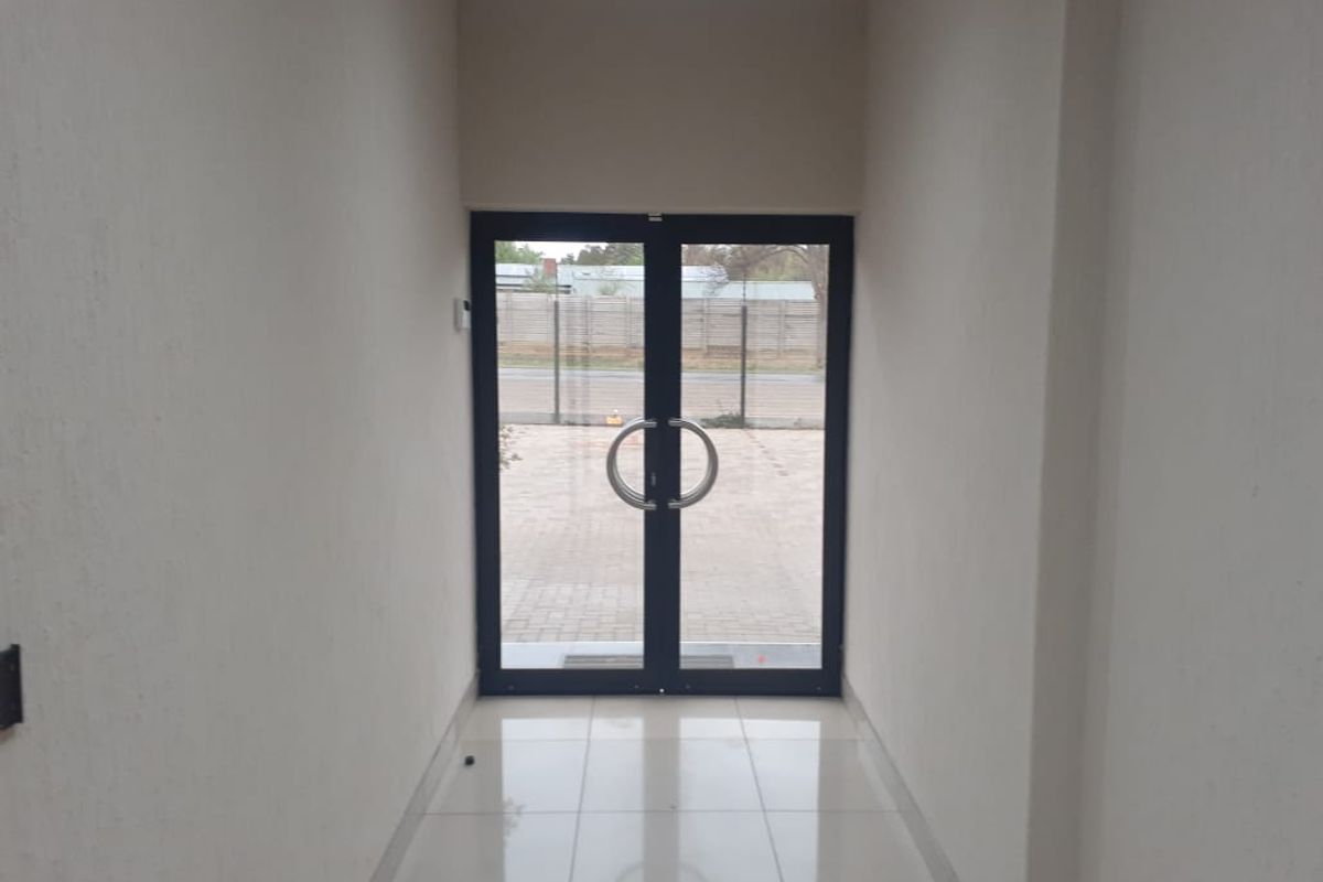 A clean and bright office entrance featuring double glass doors, neutral wall finishes, and polished floor tiles.