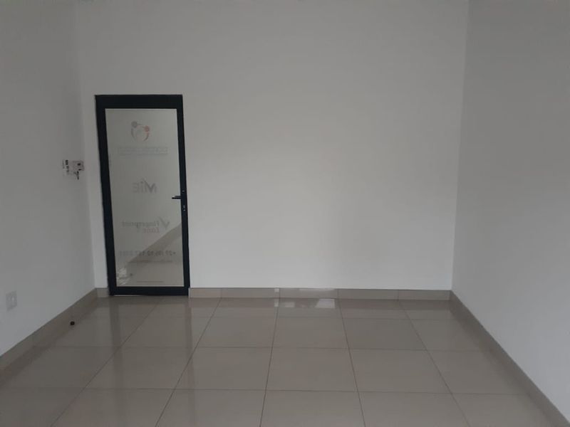 A clean, empty office space featuring neutral tiled flooring and a glass-panelled entrance door, providing a versatile environment for professional use.