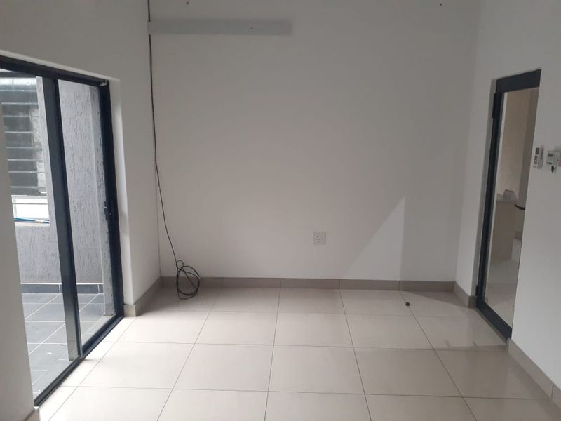 A bright, empty office space featuring neutral tiled flooring, clean white walls, and direct access to an outdoor area through a sliding glass door.