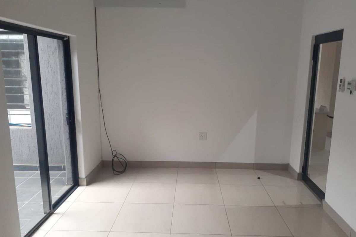 A bright, empty office space featuring neutral tiled flooring, clean white walls, and direct access to an outdoor area through a sliding glass door.