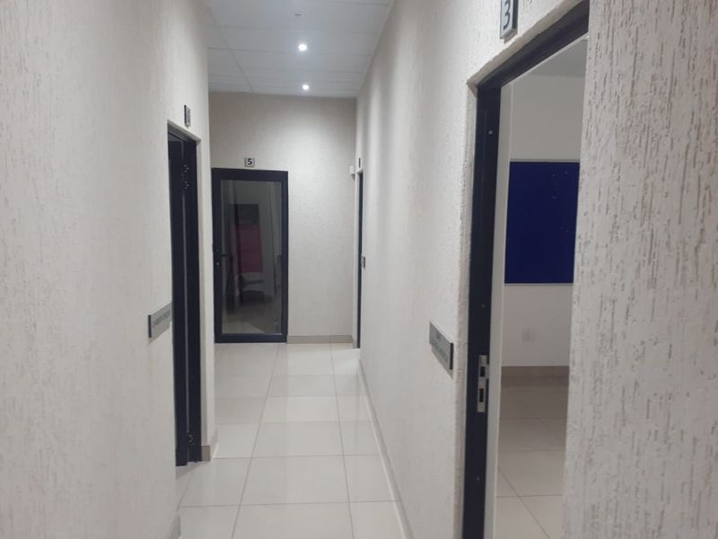 A clean, well-lit office hallway featuring tiled floors, textured walls, and multiple doorways leading to individual office spaces.
