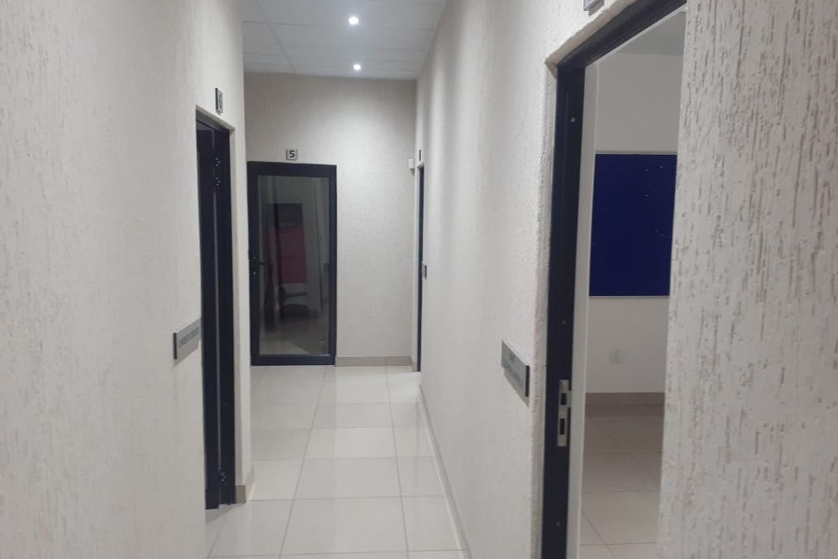 A clean, well-lit office hallway featuring tiled floors, textured walls, and multiple doorways leading to individual office spaces.