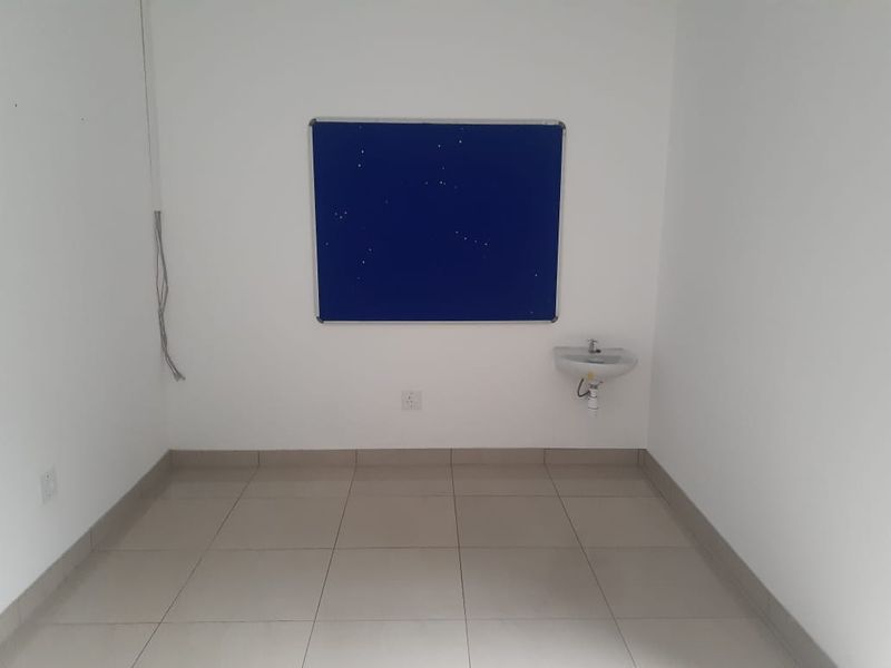 A vacant office space featuring tiled flooring, a wall-mounted basin, and exposed electrical wiring, offering a clean and functional layout for professional use.