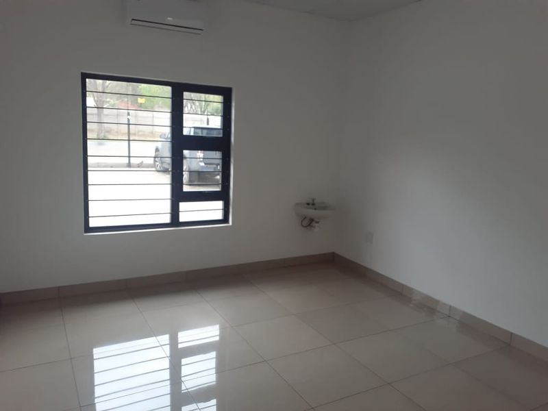 A clean, empty office space featuring tiled flooring, a wall-mounted basin, and an air conditioning unit, suitable for professional use.