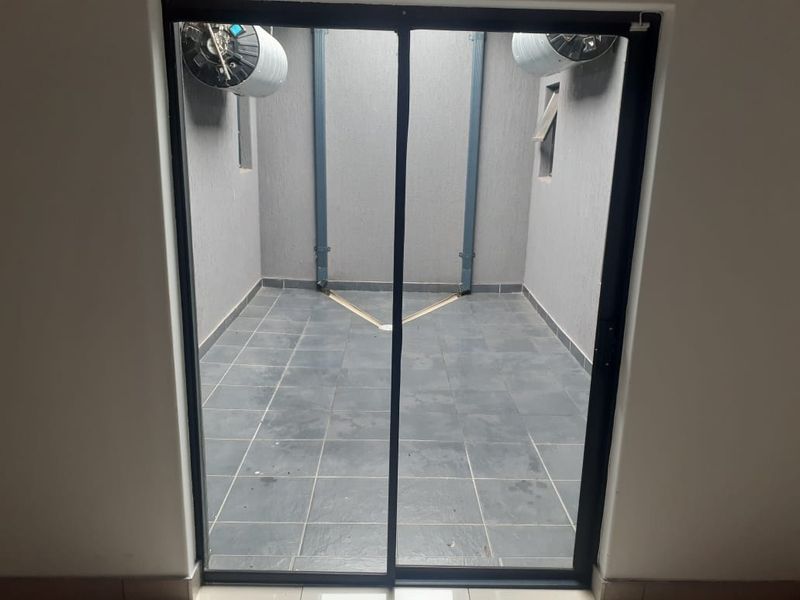 A clean, tiled utility courtyard or service area featuring dual electric water heaters and a sliding glass door entrance.
