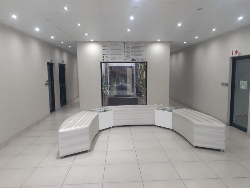 A well-lit commercial building lobby or hallway featuring tiled floors, directory signage, and access to multiple office suites.