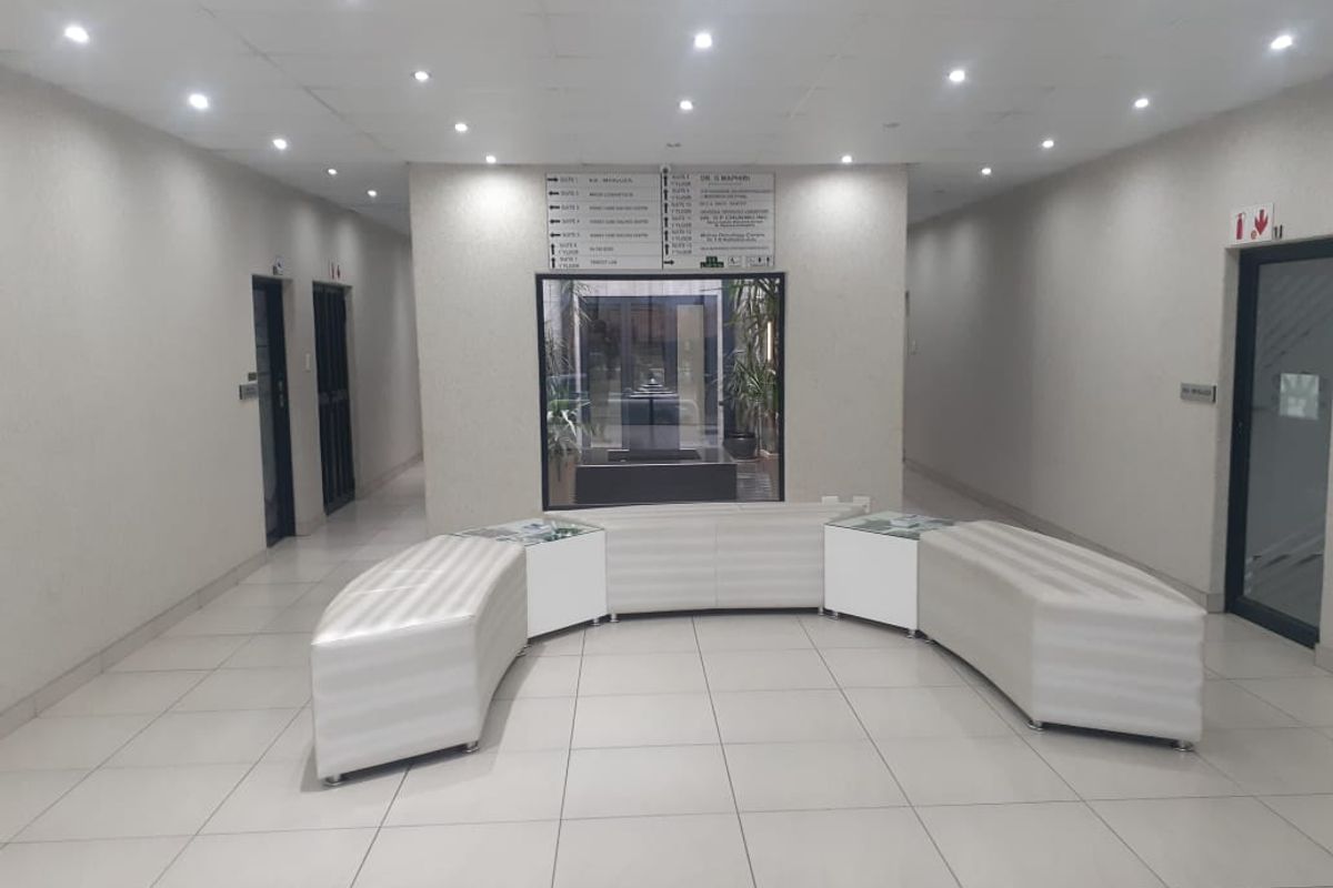 A well-lit commercial building lobby or hallway featuring tiled floors, directory signage, and access to multiple office suites.