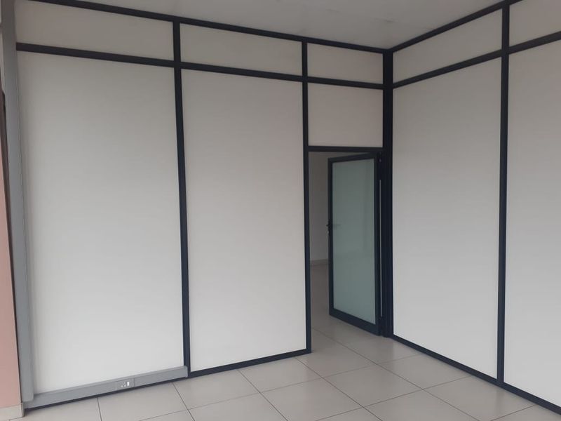 A clean, empty office space featuring modular partition walls, tiled flooring, and a glass panel door, suitable for professional use.