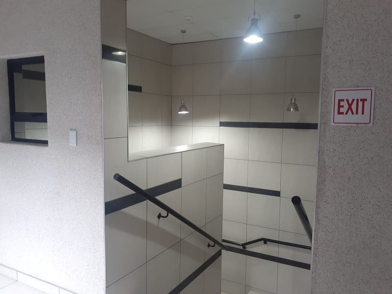 A modern commercial hallway featuring tiled walls, a staircase with a black handrail, and pendant lighting.