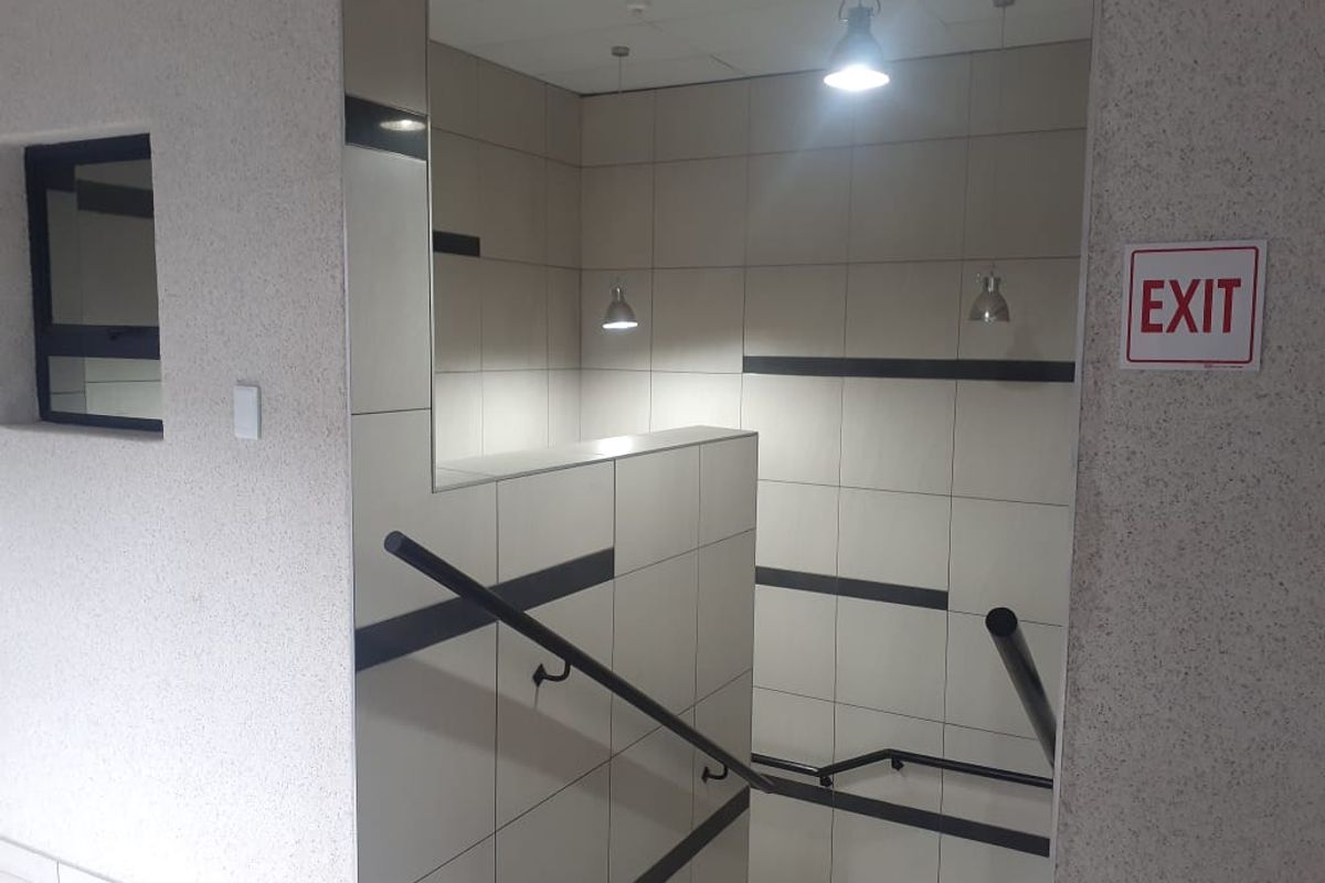A modern commercial hallway featuring tiled walls, a staircase with a black handrail, and pendant lighting.