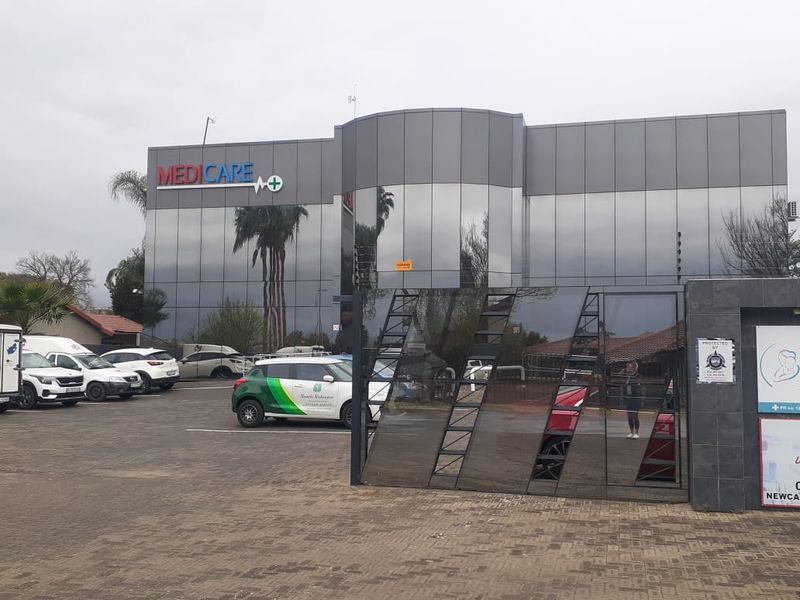Front exterior view of a modern commercial building featuring a glass facade, paved parking area, and secure gated entrance.