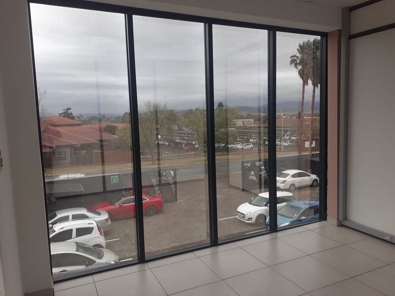 Bright and spacious office area featuring large floor-to-ceiling windows with views of the parking area and surrounding commercial property.