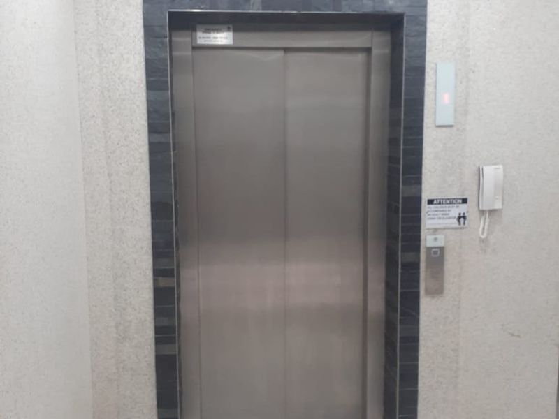 A clean commercial hallway featuring a stainless steel elevator with a decorative stone tile surround and integrated intercom system.