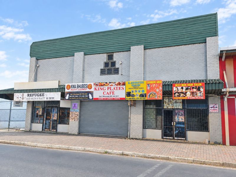 Front elevation of a multi-tenant industrial or commercial building featuring multiple storefronts, security shutters, and signage along a paved street.